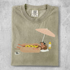 T-shirt with a dog wearing sunglasses, relaxing under a beach umbrella.