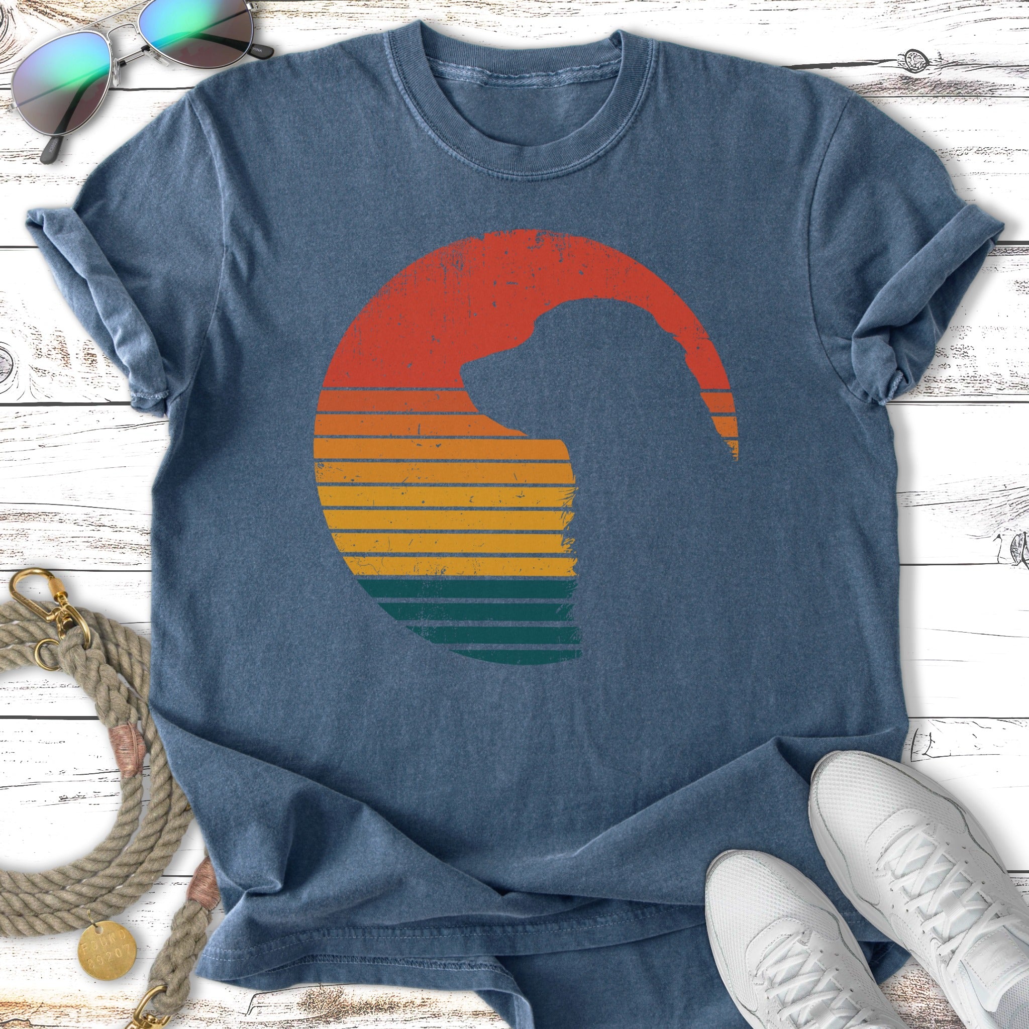 Silhouette of a dog's head within a sunset circle on a blue t-shirt.
