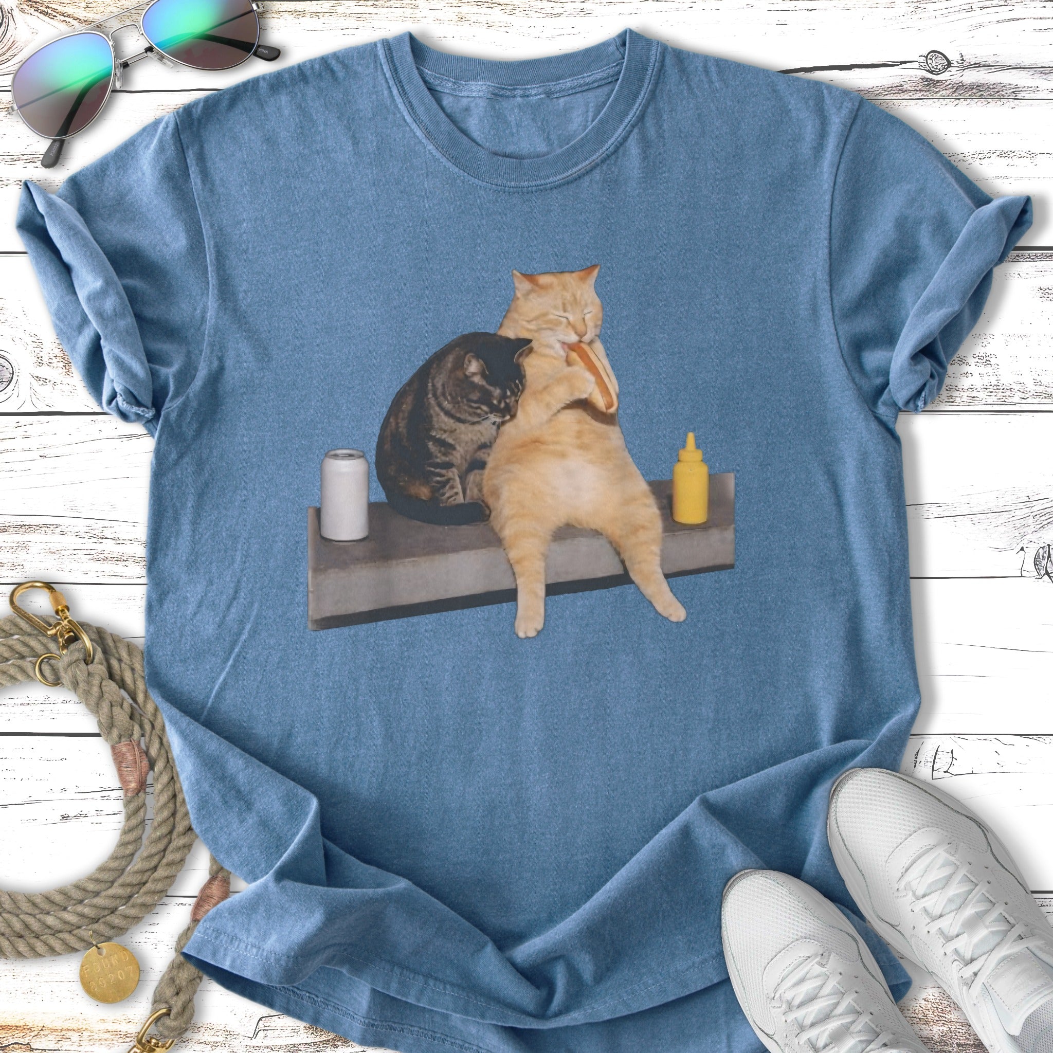 Two cats eating a hot dog on a blue t-shirt.