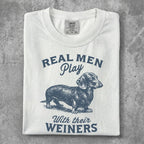 White t-shirt with blue dachshund graphic and "Real Men Play With Their WIENERS" text.