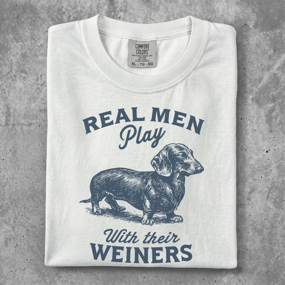 White t-shirt with blue dachshund graphic and "Real Men Play With Their WIENERS" text.