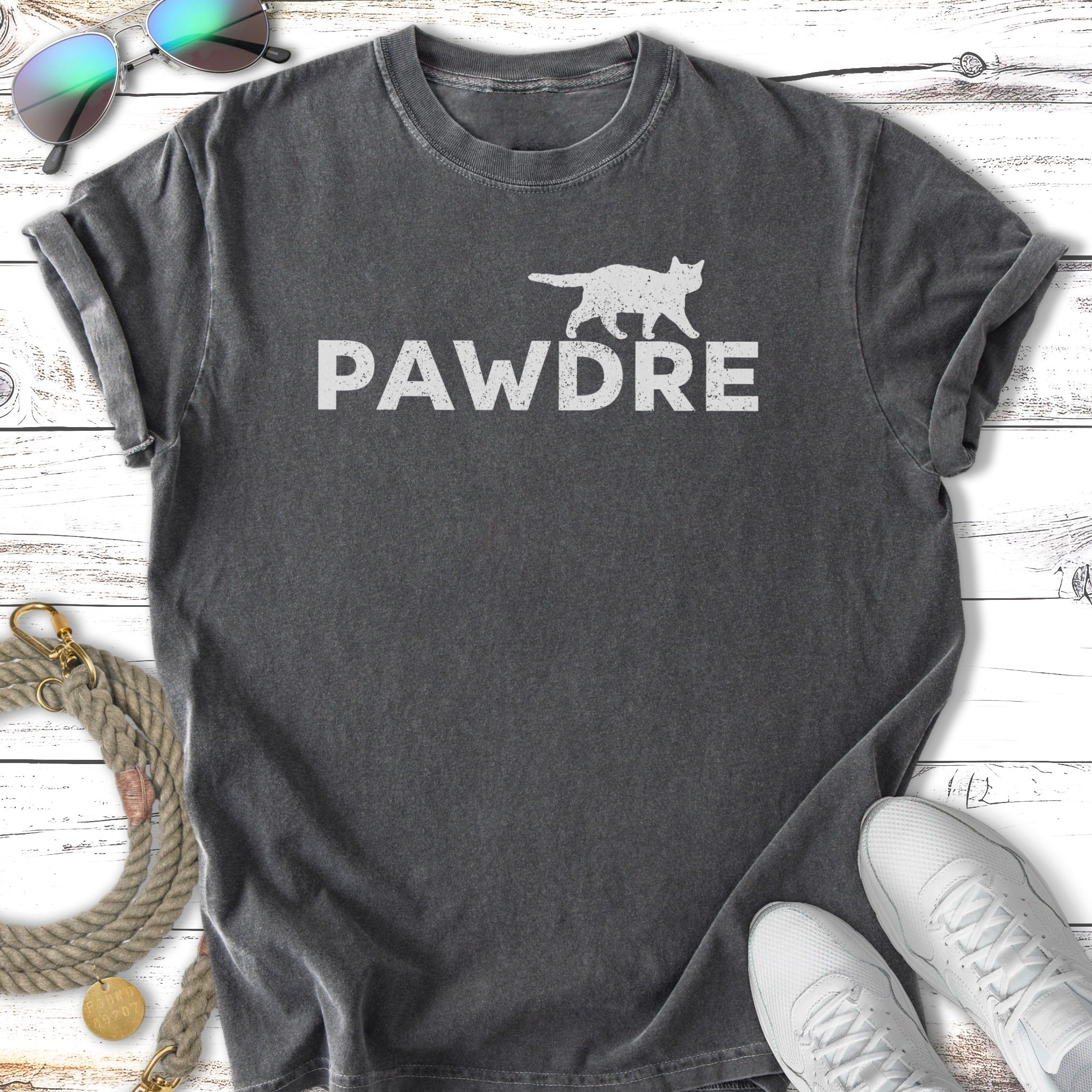 Dark grey t-shirt with "PAWDRE" text in white, flat lay with sunglasses and sneakers.
