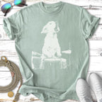 White dog playing drums on a light green t-shirt.