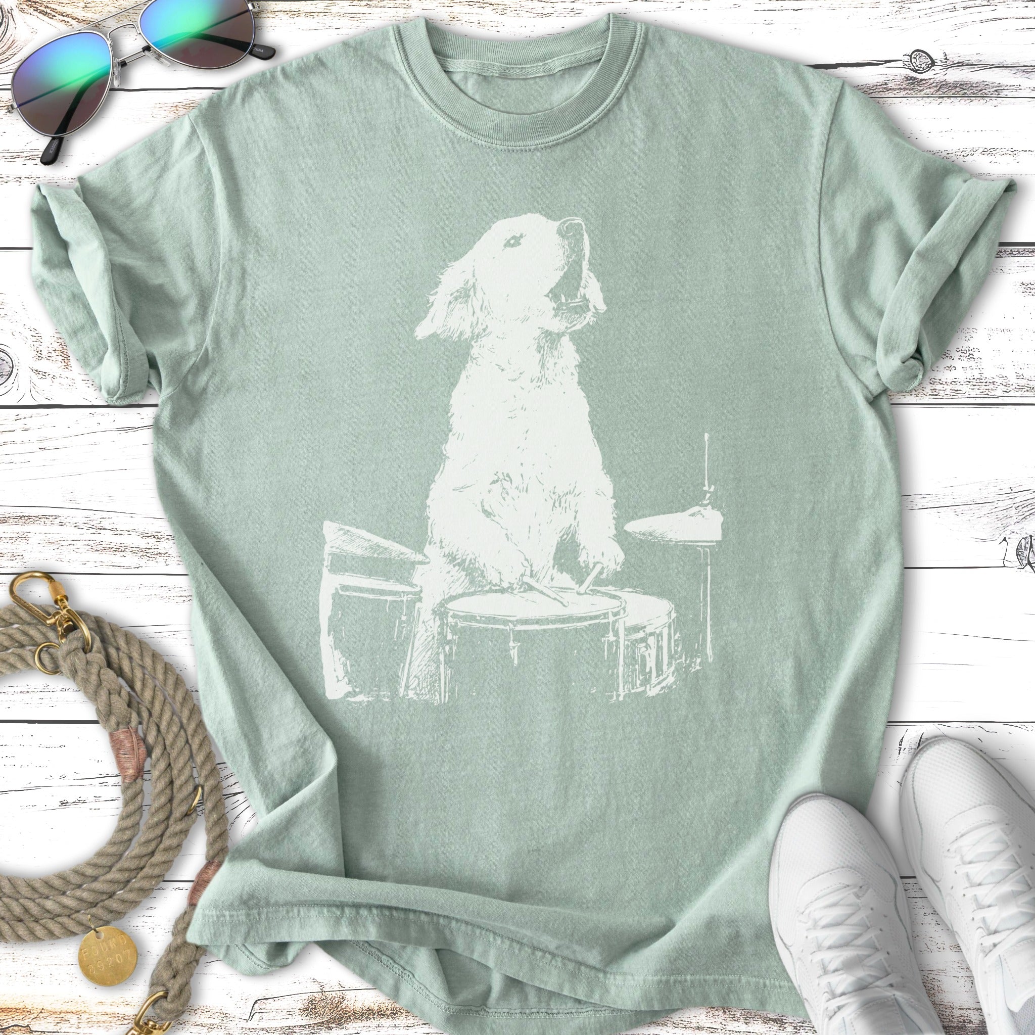 White dog playing drums on a light green t-shirt.