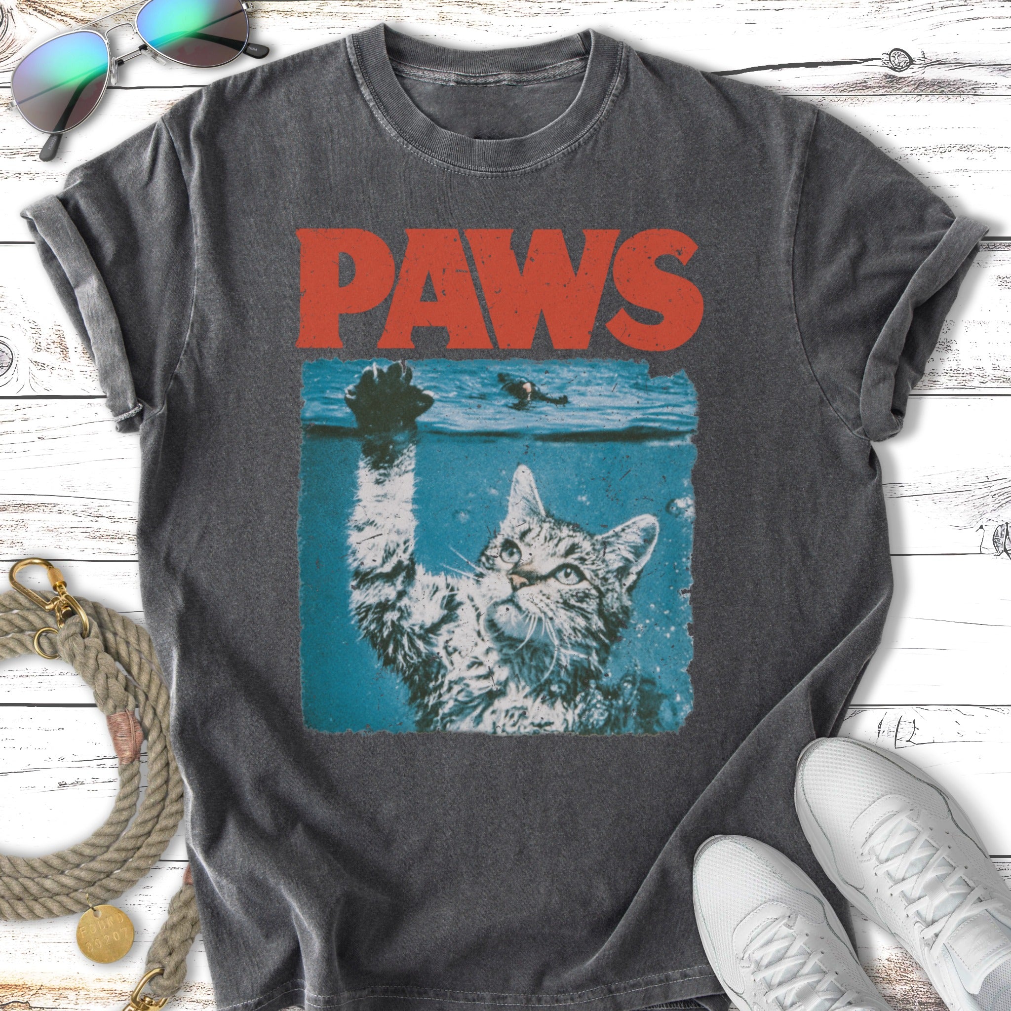 Cat reaching out of water with "PAWS" text above, on a dark t-shirt.