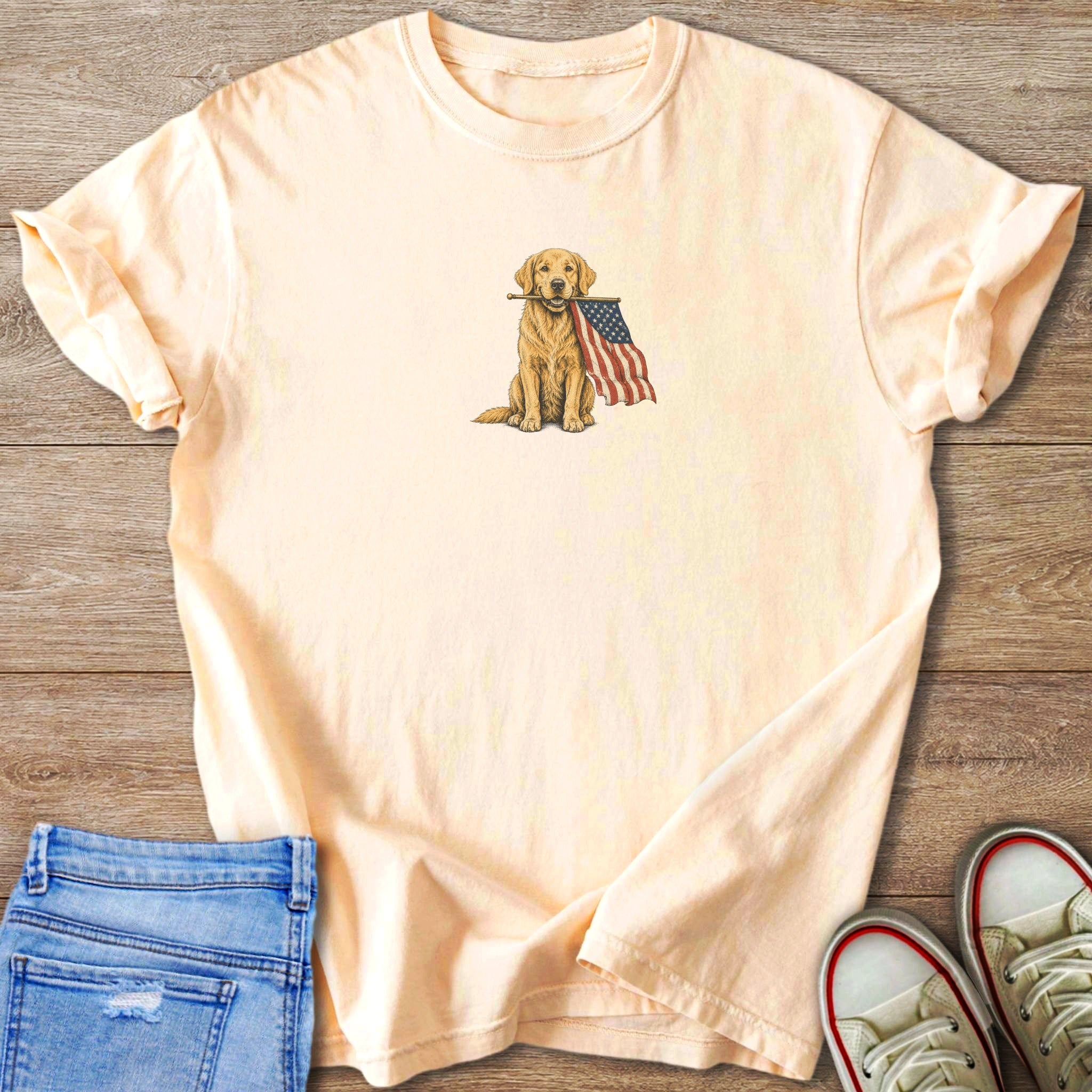 Peach t-shirt with a golden retriever holding an American flag in its mouth.