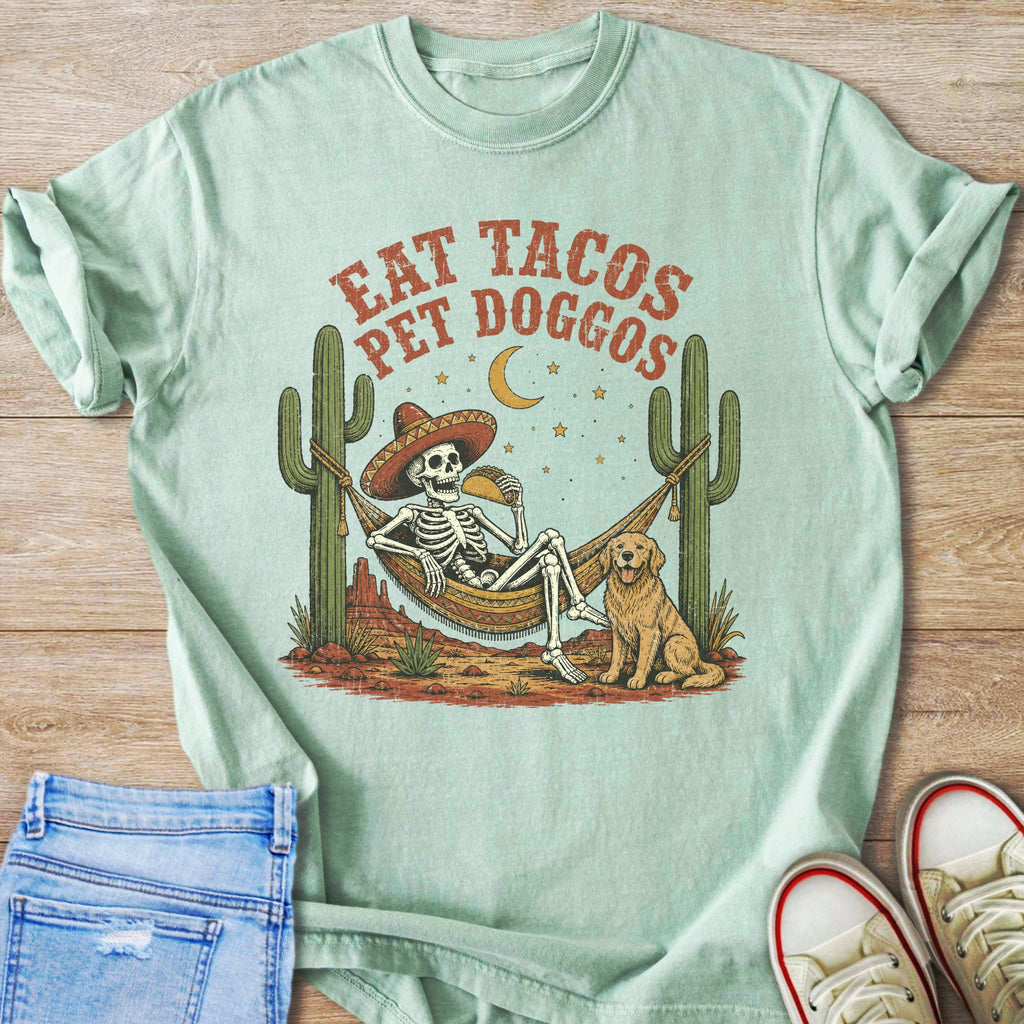 Skeleton in sombrero eating taco in hammock with dog and cacti.