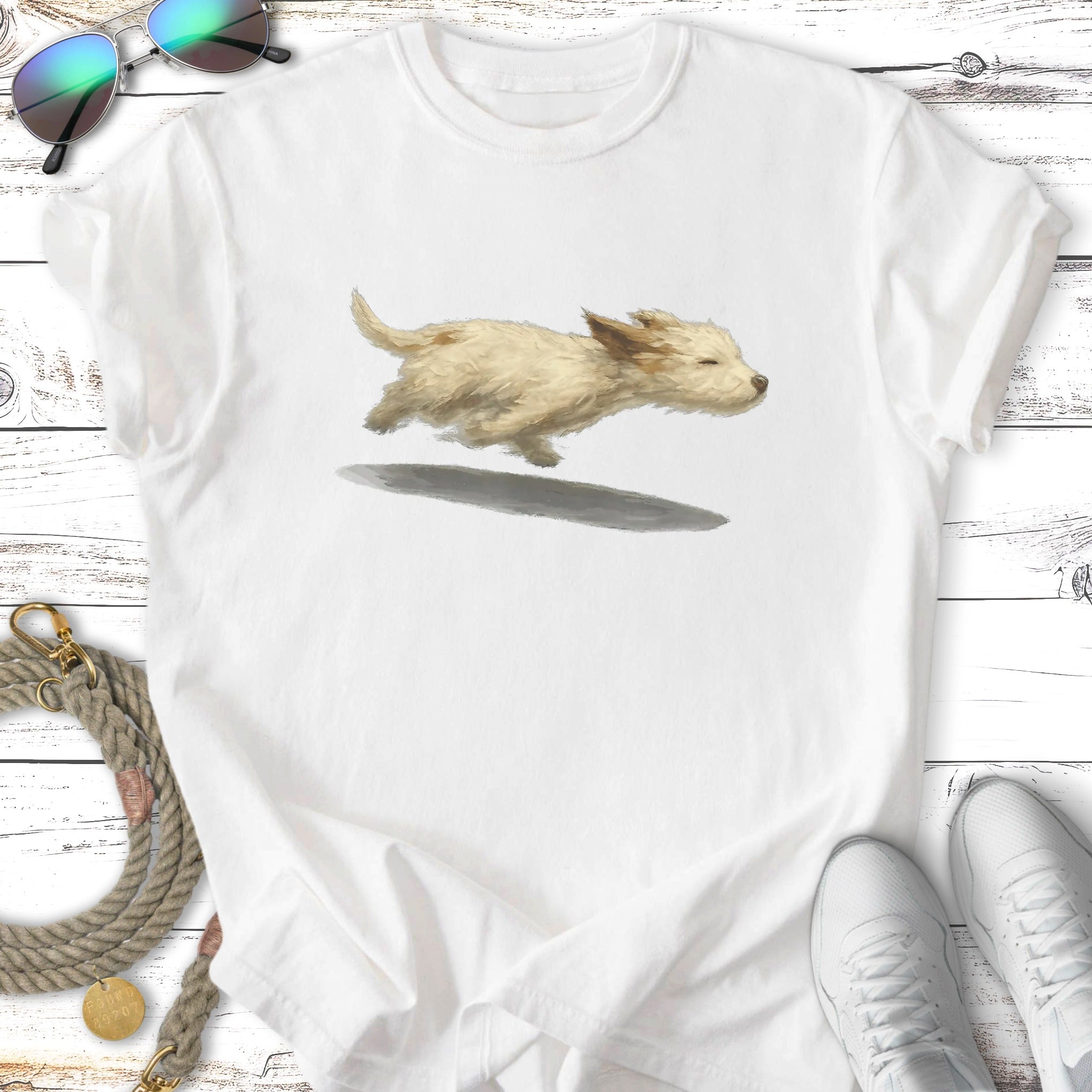 Cream-colored puppy running with a shadow beneath it, on a white t-shirt.