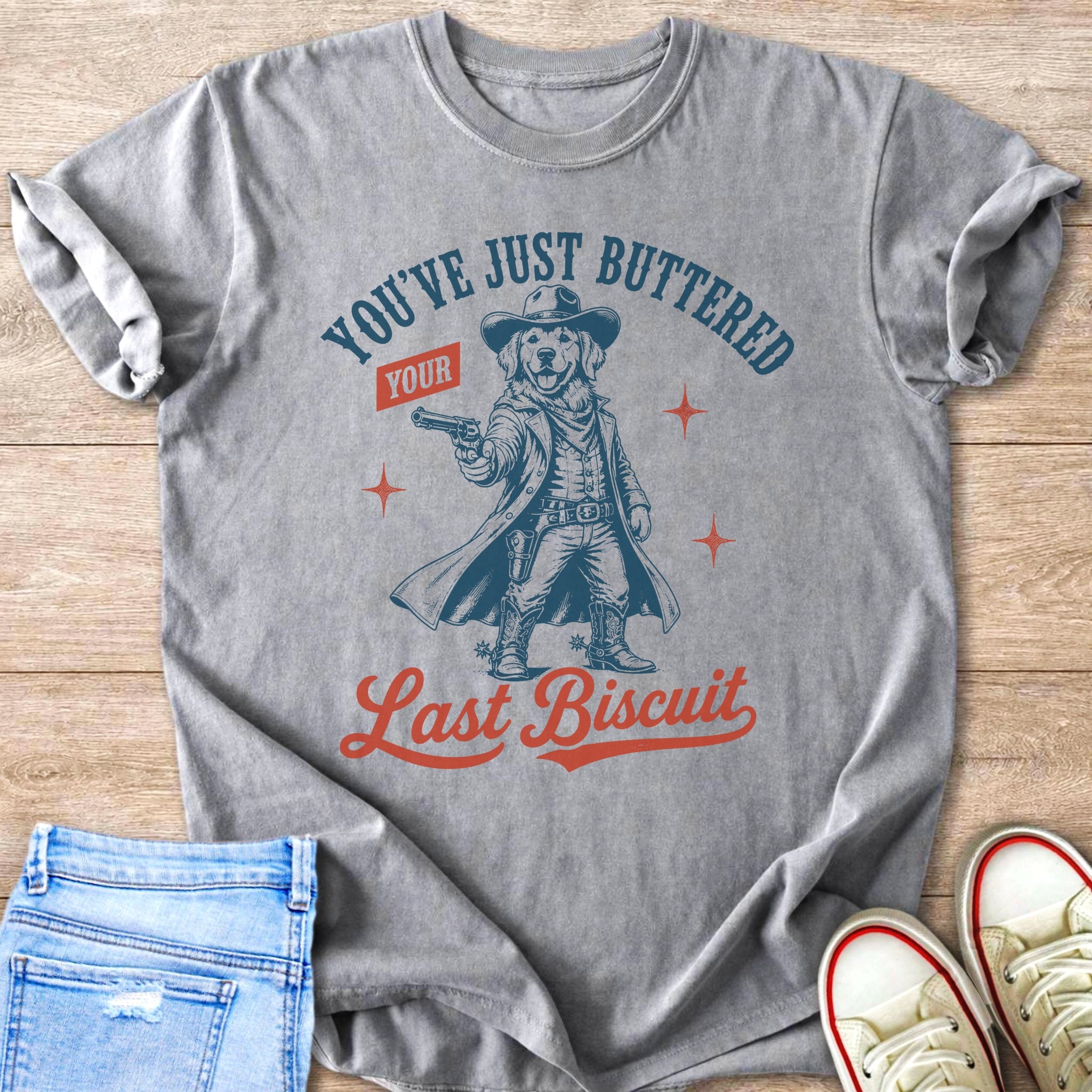T-shirt with graphic of a dog in cowboy attire holding a gun and text "You've Just Buttered Your Last Biscuit."