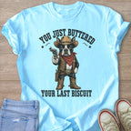 Light blue t-shirt graphic of a Boston Terrier dressed as a cowboy holding a gun.