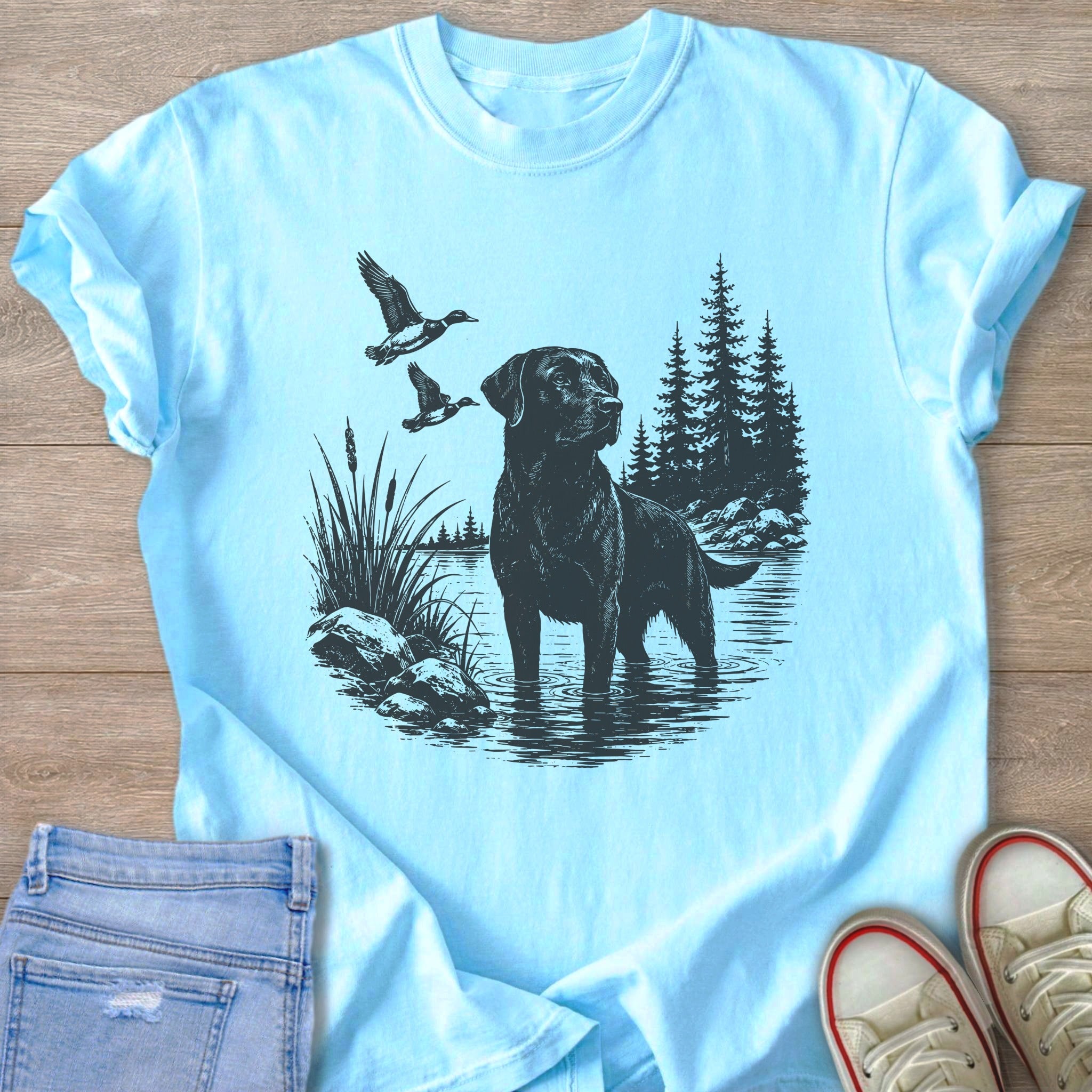 Black Labrador standing in water with ducks flying overhead and trees in background.
