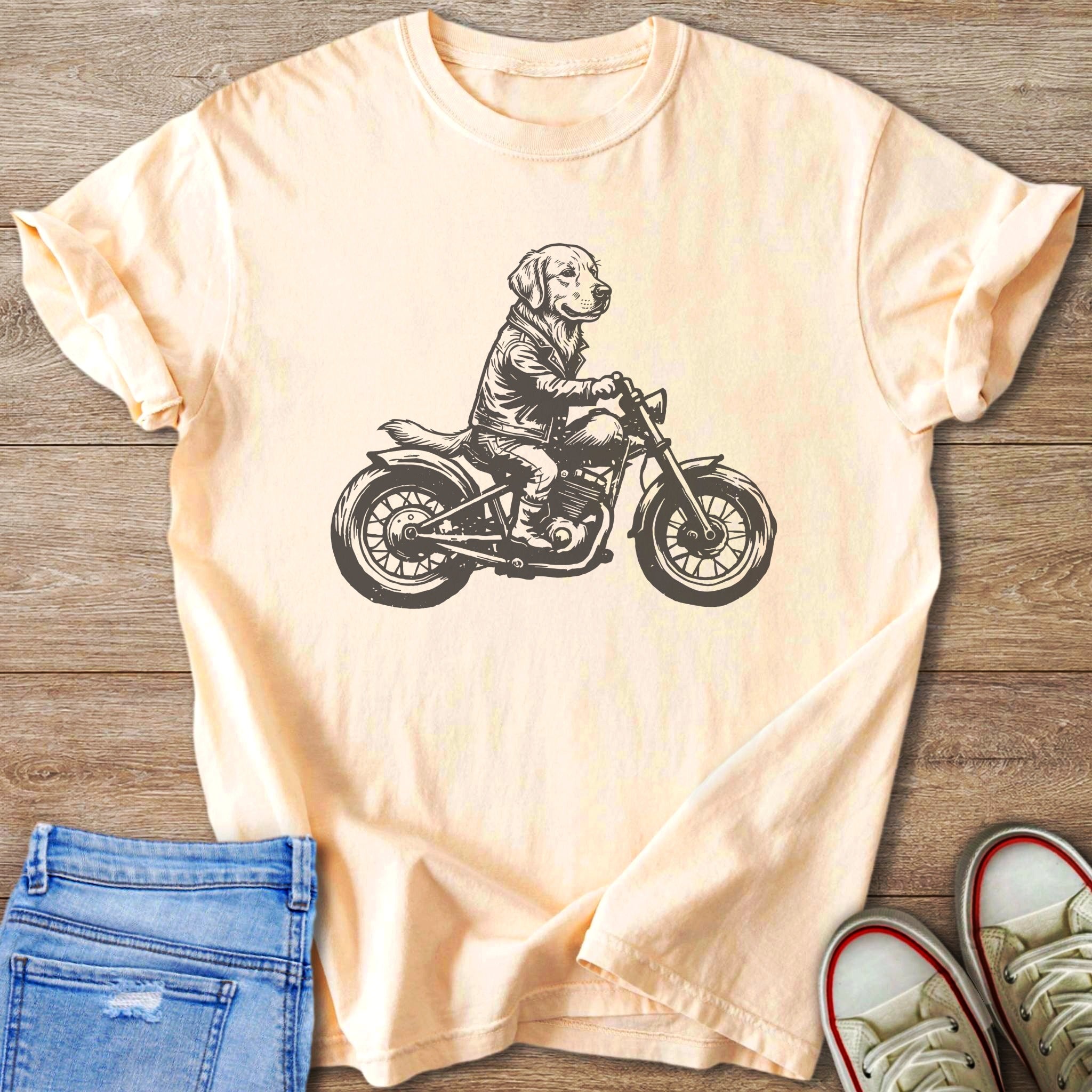 Black and white sketch of a dog wearing a jacket riding a motorcycle on a peach t-shirt.