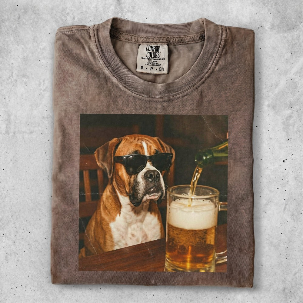 Boxer dog wearing sunglasses sitting at a table with a beer.