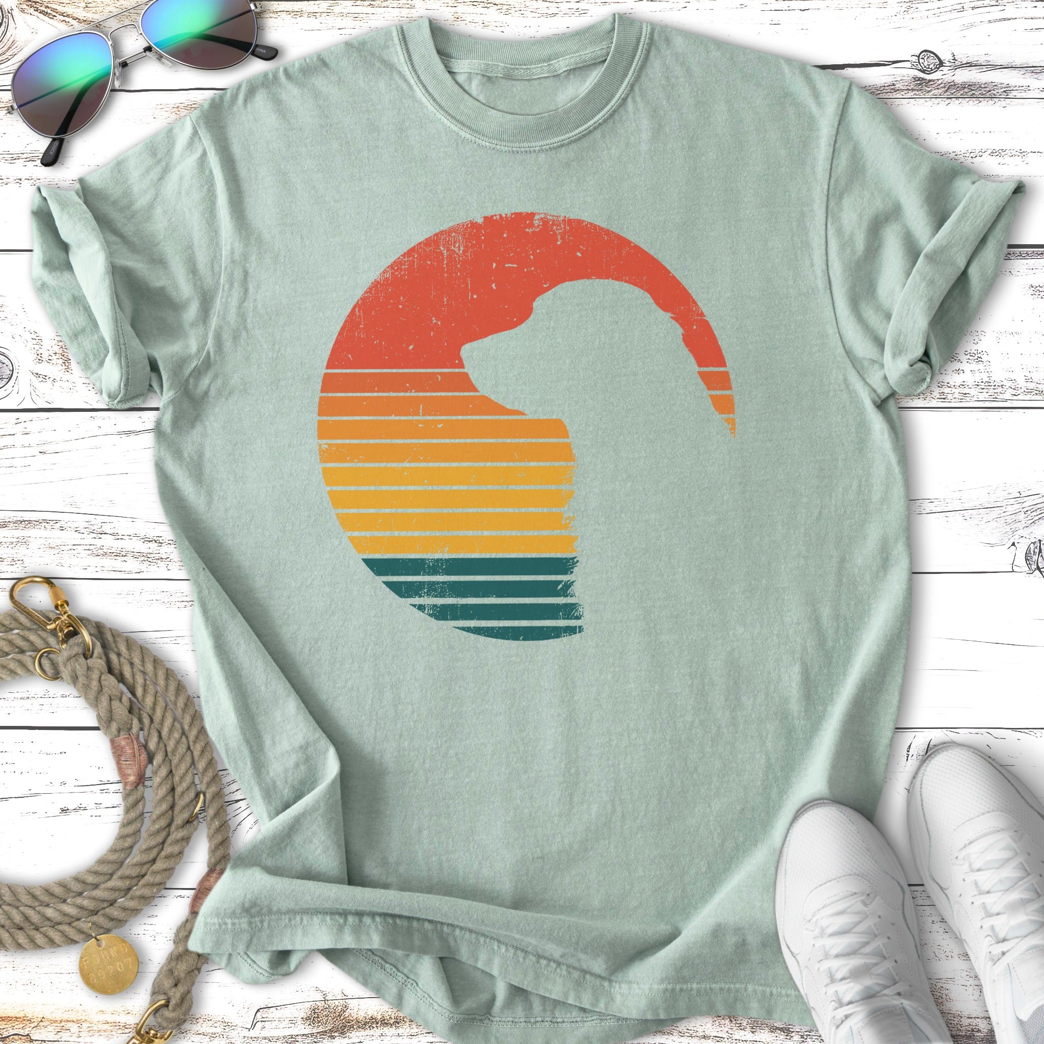 Silhouette of a dog within a retro sunset circle on a light green t-shirt.