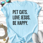 Light blue t-shirt with "PET CATS. LOVE JESUS. BE HAPPY." text.