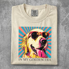 Cream t-shirt with a golden retriever wearing sunglasses, tongue out, against a colorful background.