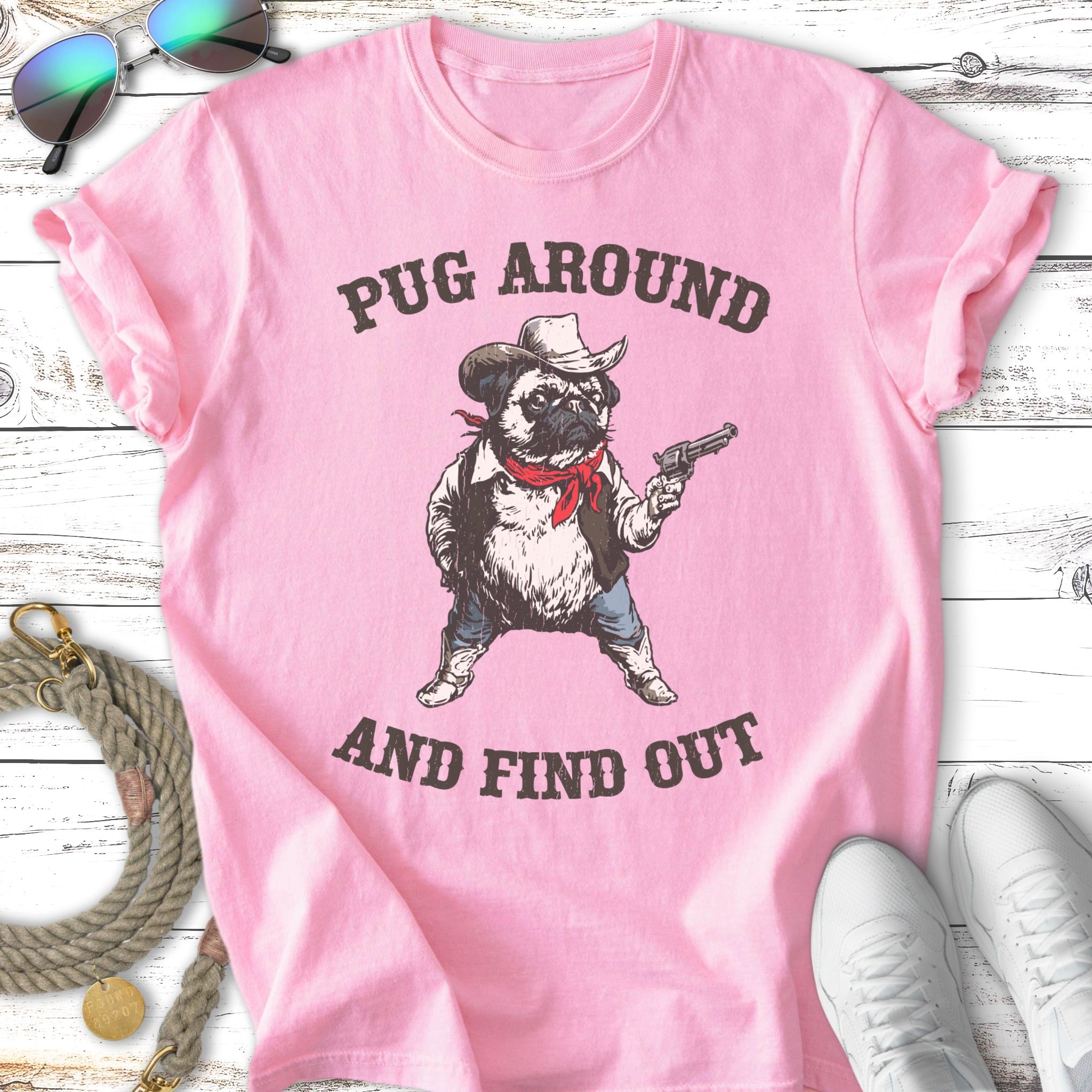 Pink t-shirt with pug in cowboy outfit holding a gun, text reads "Pug Around and Find Out".