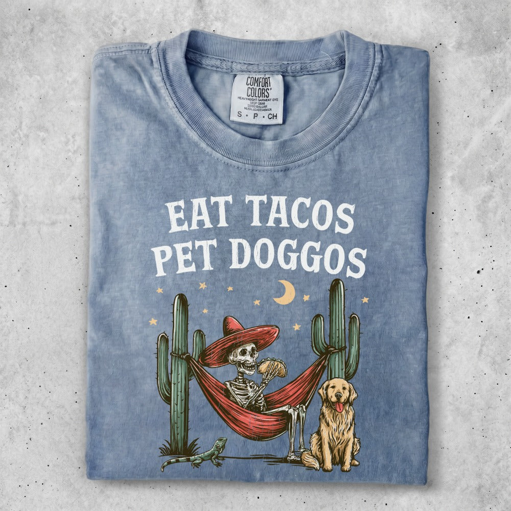 Skeleton in hammock with tacos, dog, and cacti under starry sky.