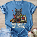 French bulldog knight holding a quilt and seam ripper, text says "WE QUILT AT DAWN".