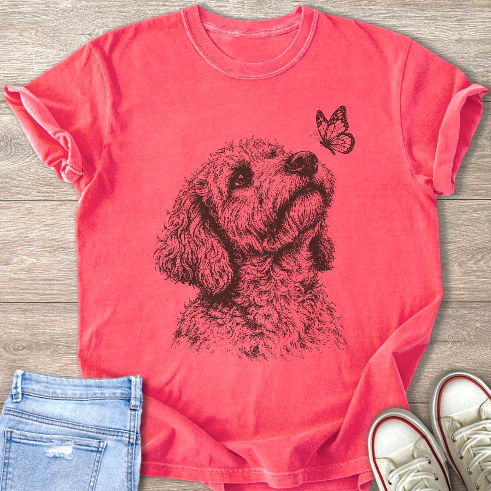 Goldendoodle dog looking up at a butterfly on a pink t-shirt.