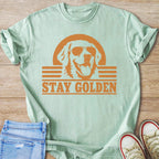 Light green t-shirt with orange graphic of golden retriever wearing sunglasses and text "STAY GOLDEN".