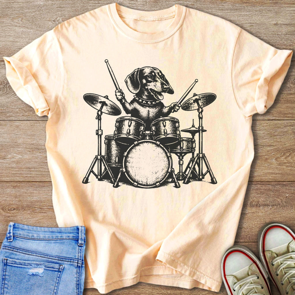 Dachshund playing a drum set on a light peach t-shirt.