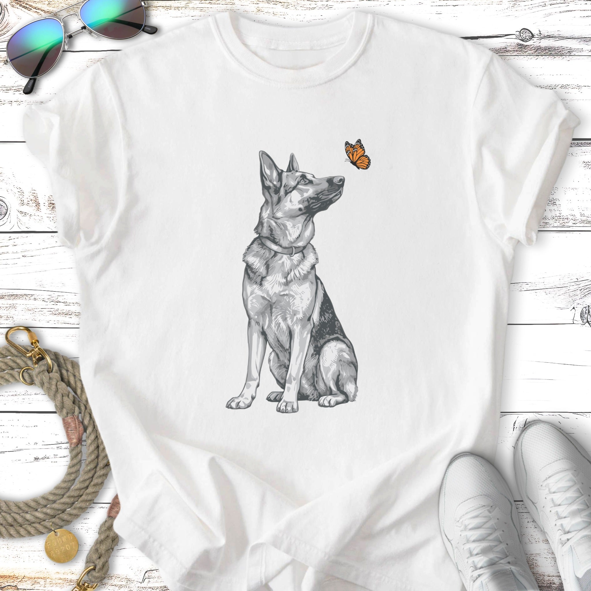 German Shepherd sitting with a butterfly above its nose on a white t-shirt.