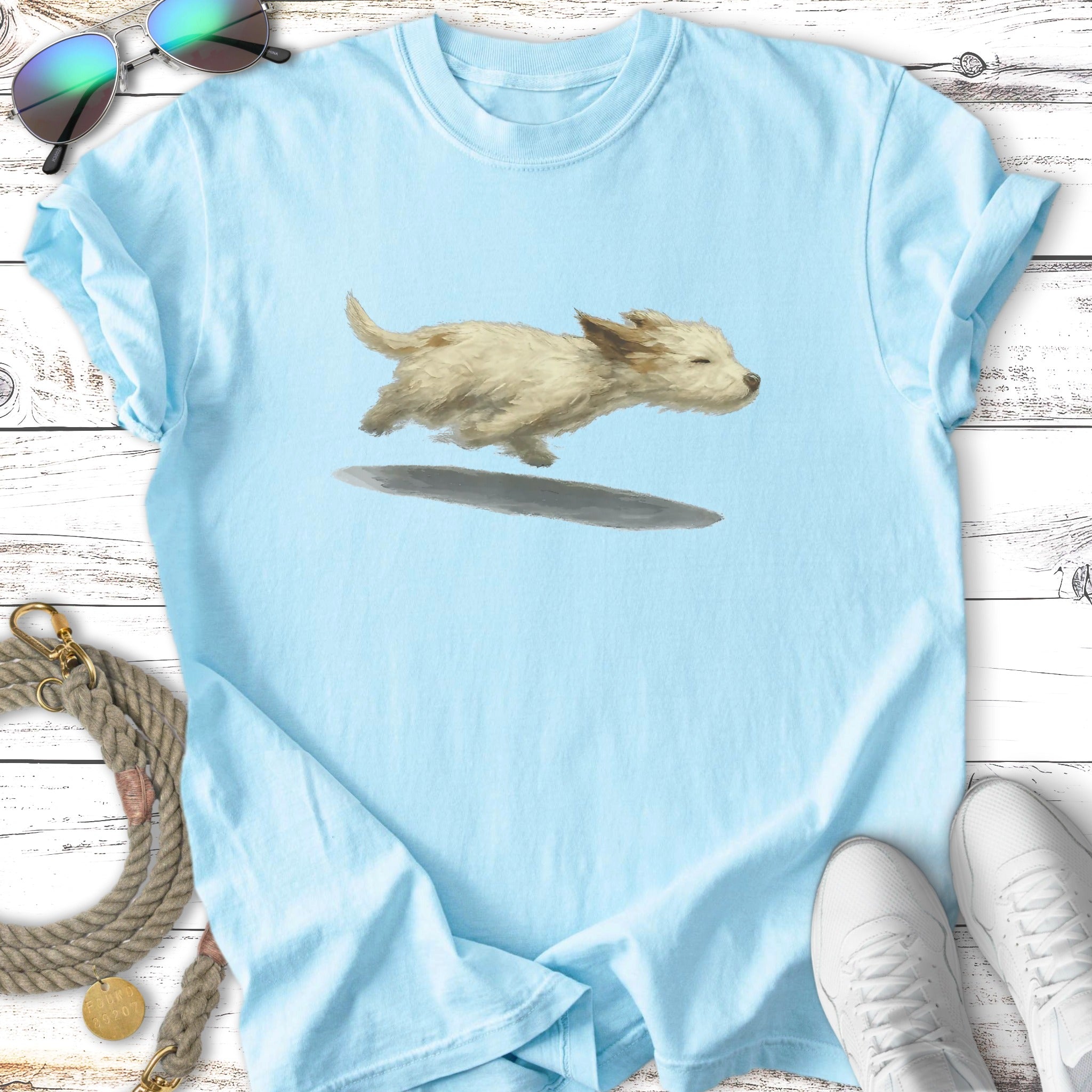 Light blue t-shirt with a fluffy white dog illustration mid-leap.