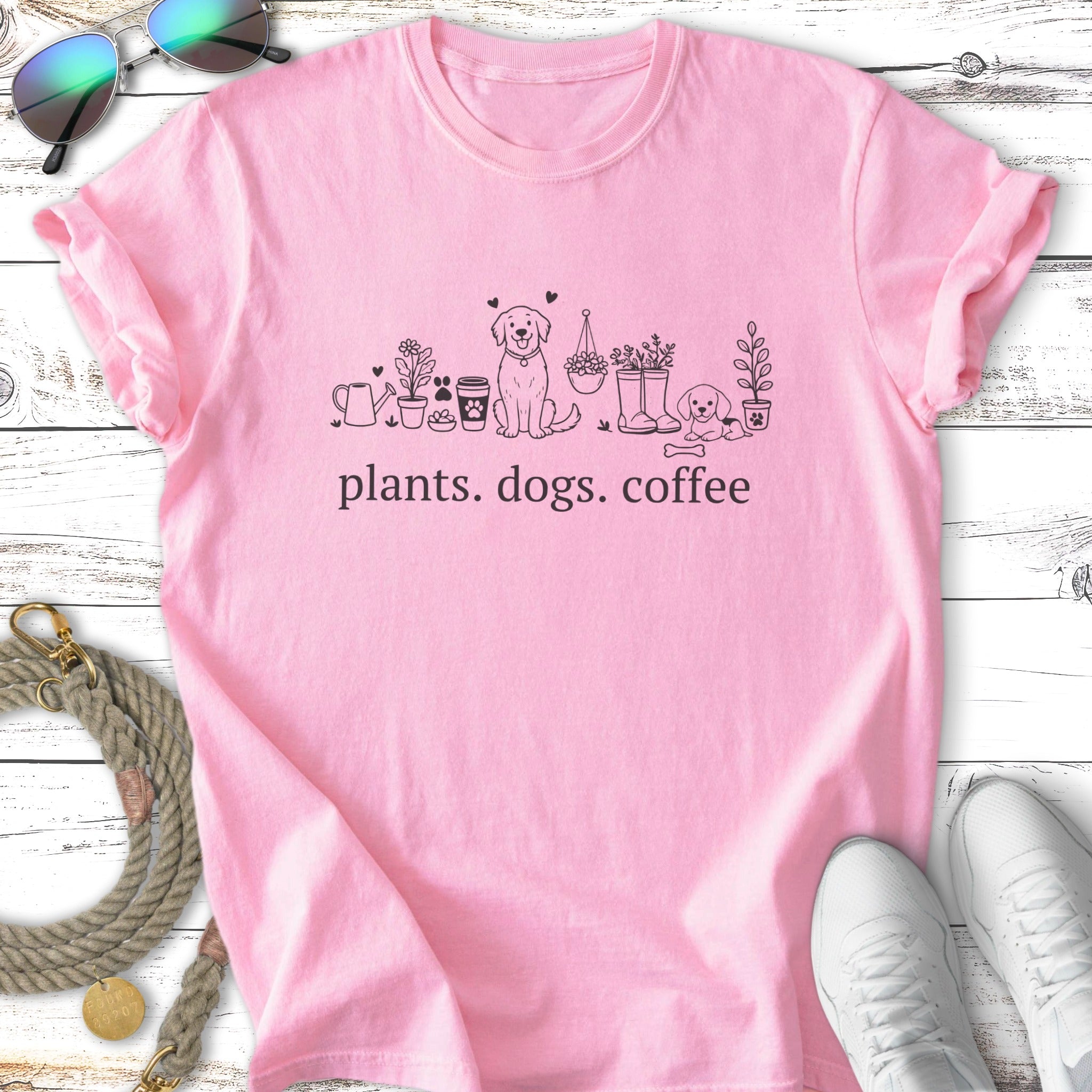 Pink t-shirt with a sketch of a dog, plants, and the text "plants. dogs. coffee."