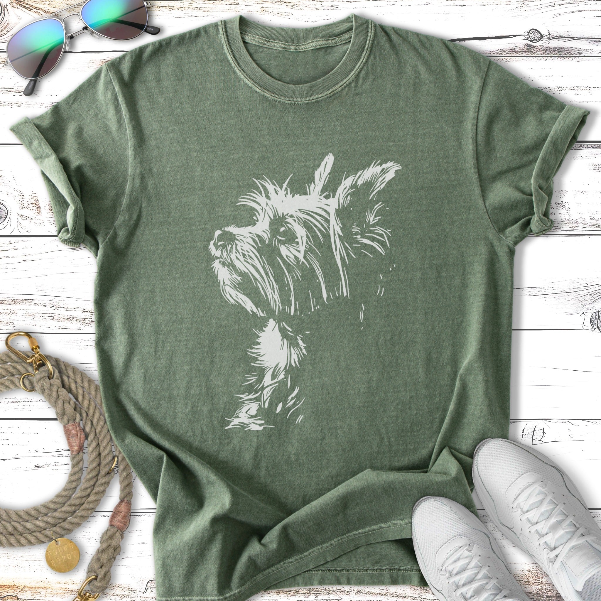 Green t-shirt with a white terrier dog silhouette on a white wooden surface.