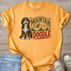Bernedoodle dog with "Mountain Doodle" graphic on an orange t-shirt.