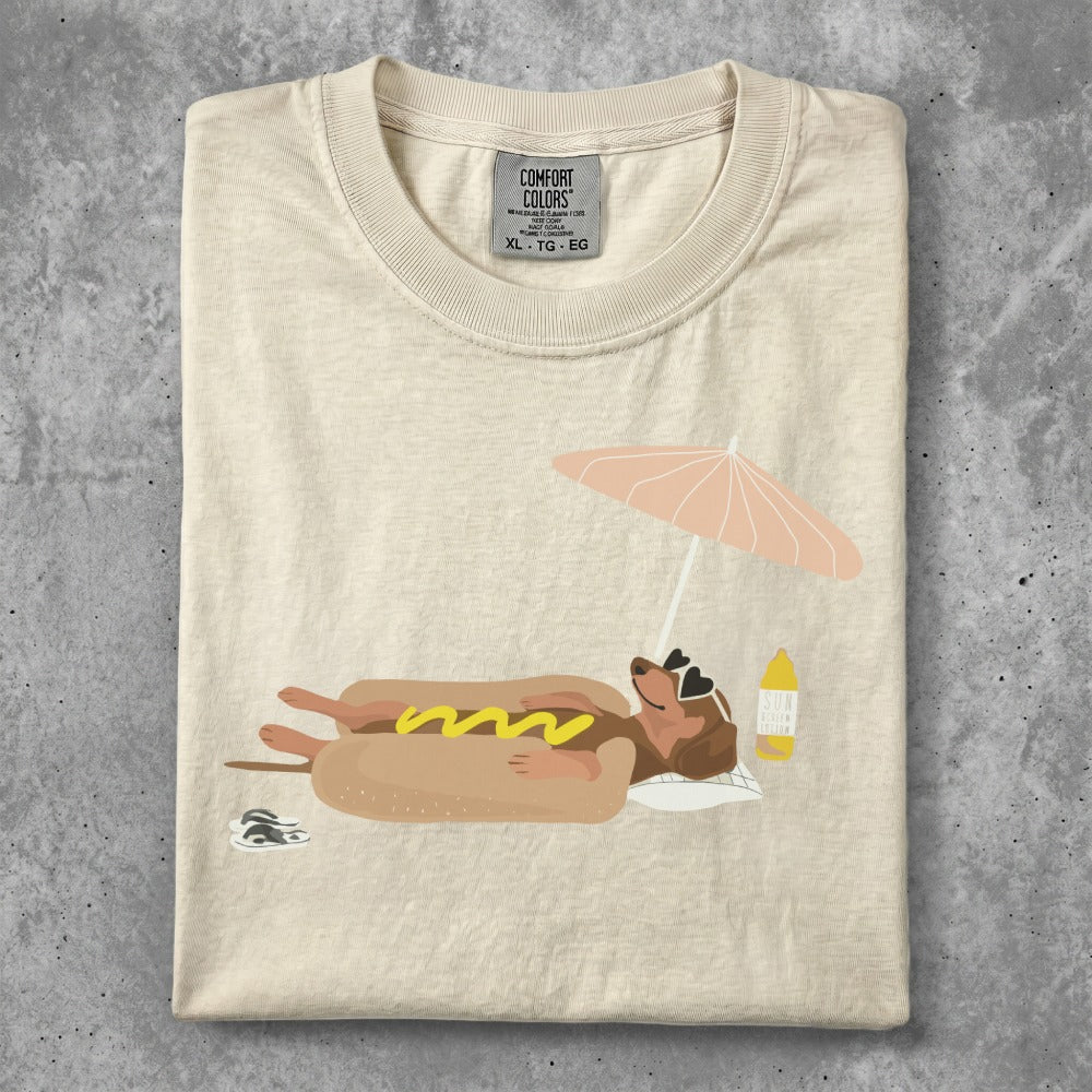 Cream t-shirt with cartoon hot dog in bun relaxing on beach under umbrella.