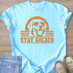 Light blue t-shirt with a distressed graphic of a golden retriever wearing sunglasses and text that reads "STAY GOLDEN".