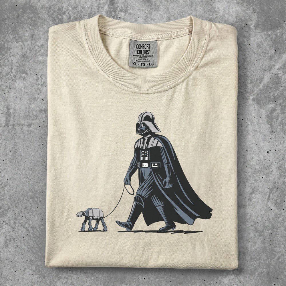 Darth Vader walking a small AT-AT on a leash, on a cream t-shirt.