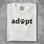 White t-shirt with black "adopt" text and paw print logo.