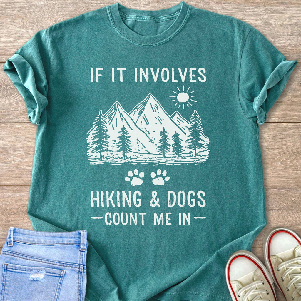 Teal t-shirt with white graphic of mountains, trees, sun, and text: "IF IT INVOLVES HIKING & DOGS -COUNT ME IN-"