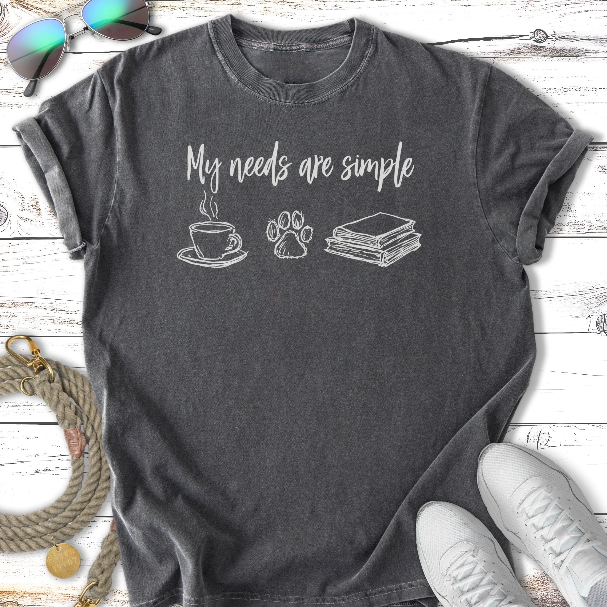 Dark grey t-shirt with "My needs are simple" and icons of coffee, paw print, and books.