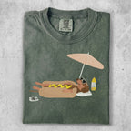 T-shirt featuring a dachshund in a bun under a beach umbrella.