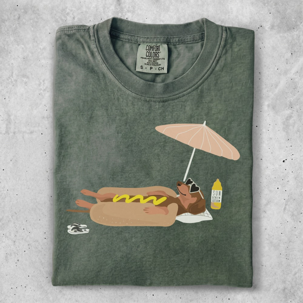 T-shirt featuring a dachshund in a bun under a beach umbrella.