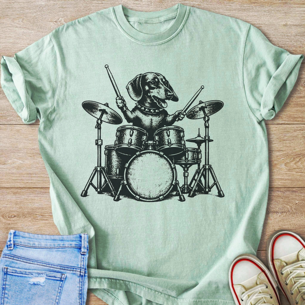 Dachshund playing drums in black ink graphic on a light green t-shirt.