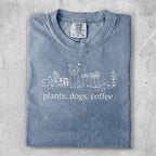 Blue t-shirt with "plants. dogs. coffee" and line drawings of plants, dogs, and coffee cup.