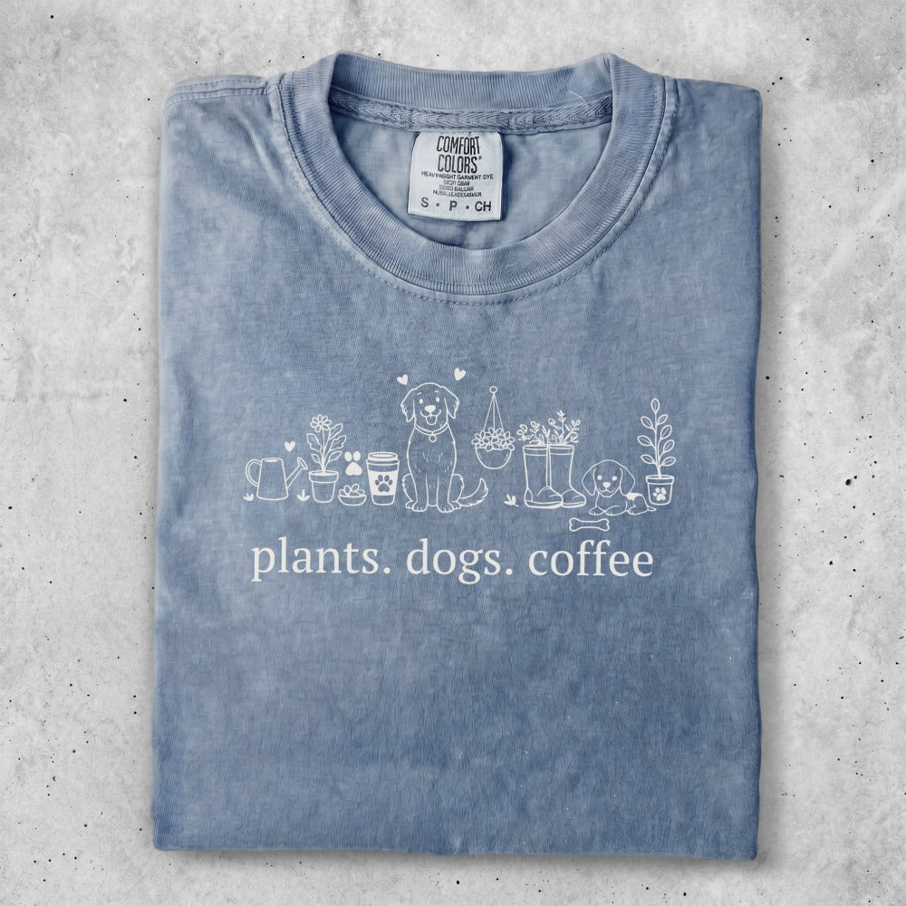 Blue t-shirt with "plants. dogs. coffee" and line drawings of plants, dogs, and coffee cup.