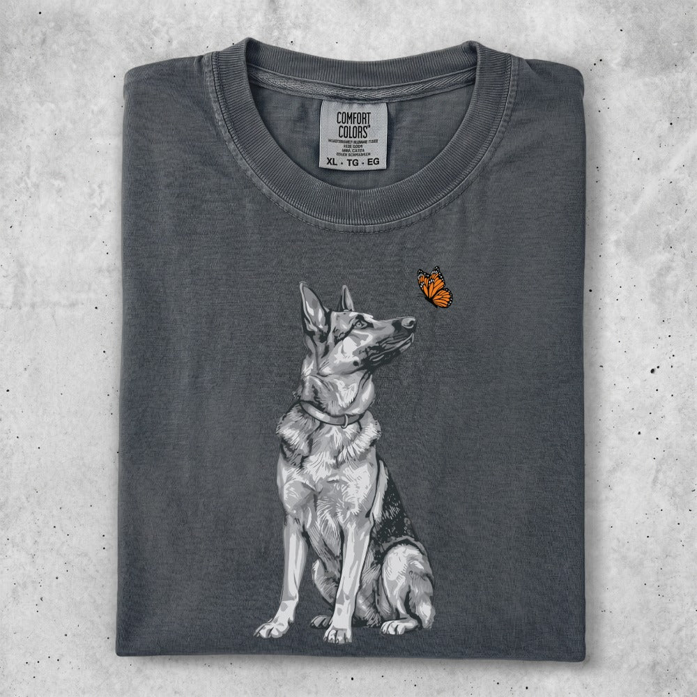 German Shepherd dog looking up at a monarch butterfly on dark grey t-shirt.