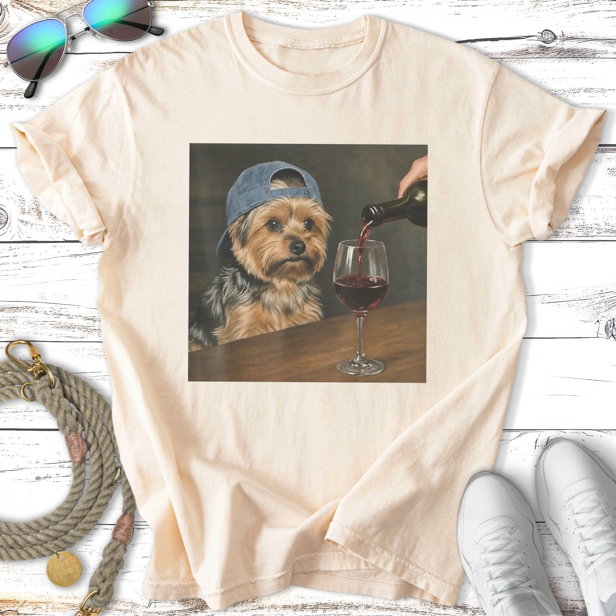 Yorkshire terrier in a baseball cap drinks red wine from a glass.