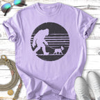 Bigfoot walking a small dog on a leash, printed on a purple t-shirt.