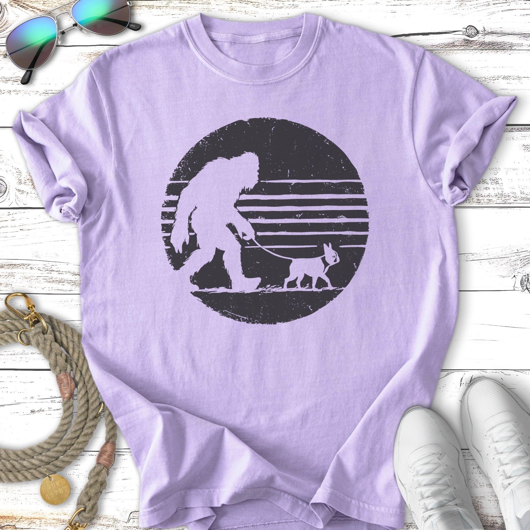 Bigfoot walking a small dog on a leash, printed on a purple t-shirt.