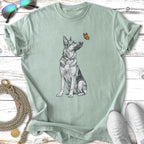 German Shepherd dog sitting, looking up at a butterfly, with sunglasses and shoes.