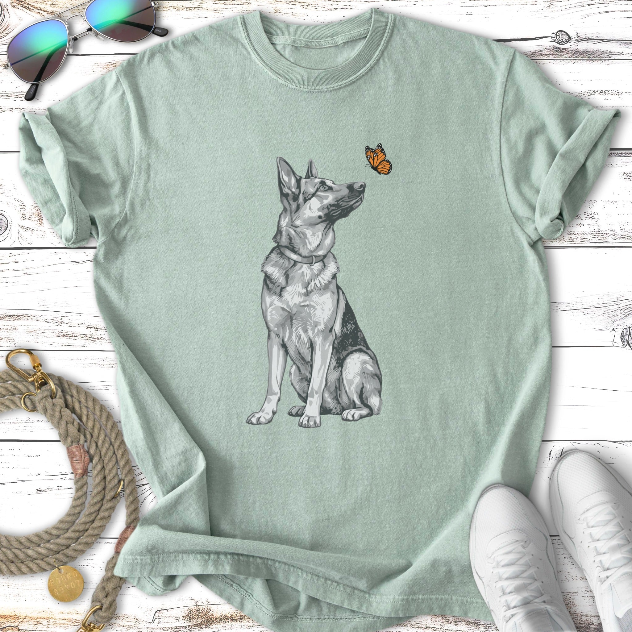German Shepherd dog sitting, looking up at a butterfly, with sunglasses and shoes.