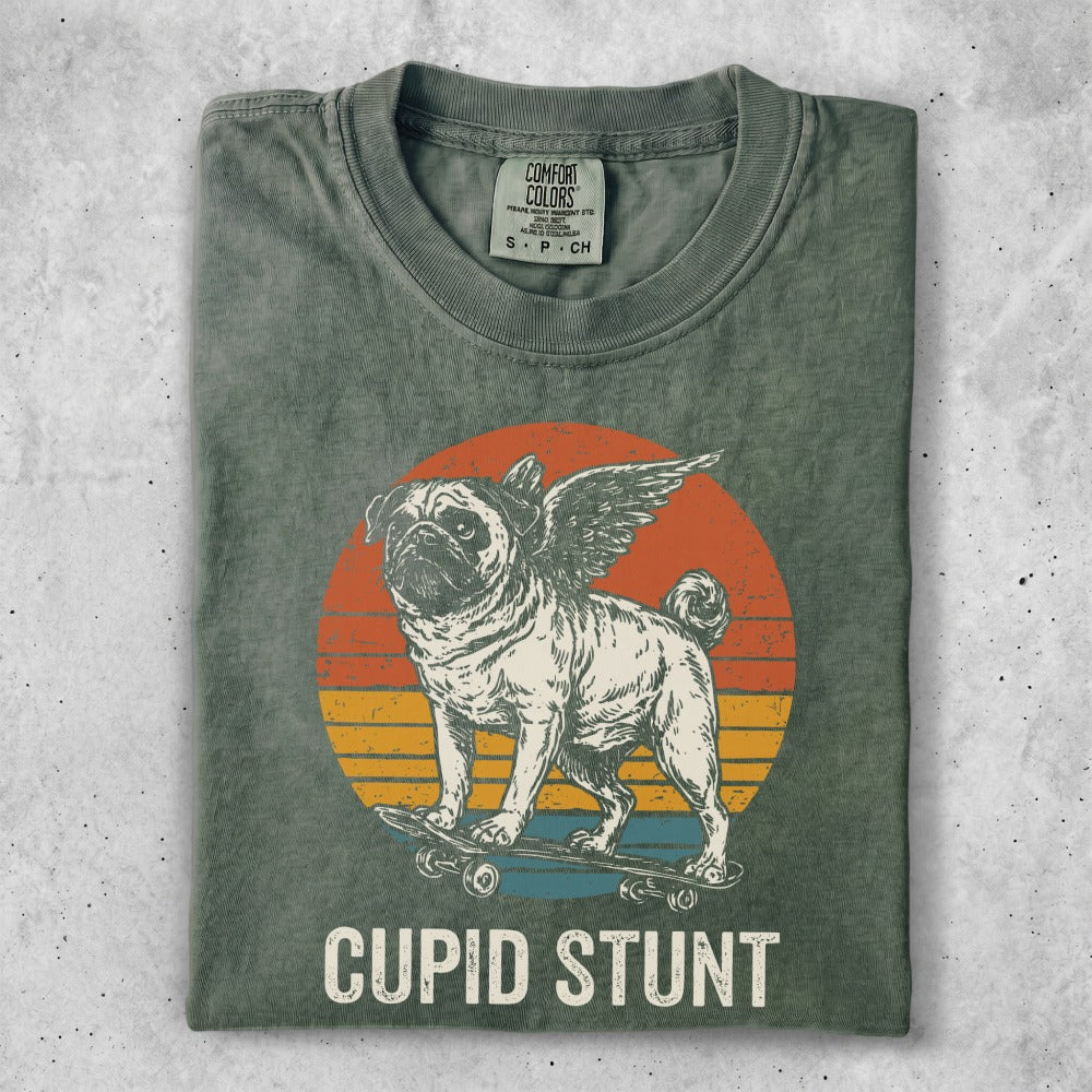 Pug with wings on skateboard, "Cupid Stunt" text, retro sunset background.
