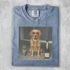 Golden retriever wearing sunglasses sits next to champagne and a glass.
